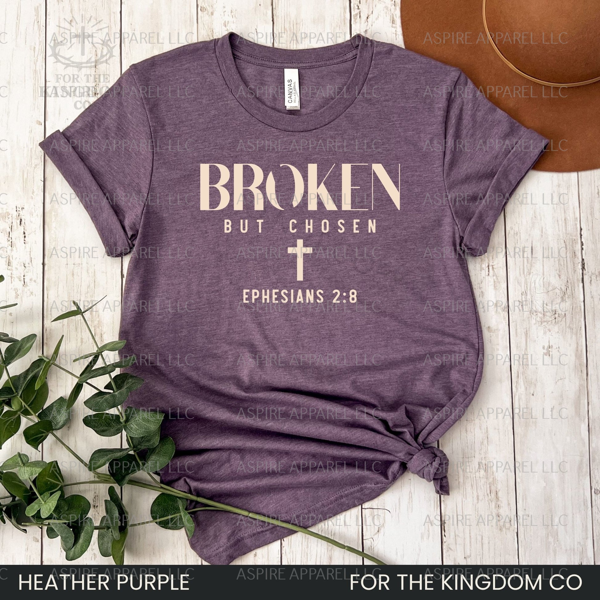 Heather purple t-shirt with 'Broken But Chosen' text and cross on a wooden surface.