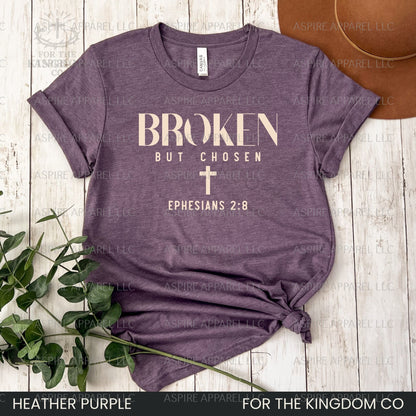 Heather purple t-shirt with 'Broken But Chosen' text and cross on a wooden surface.